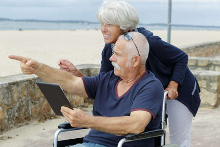 senior woman and wheelchair husband on beachの写真素材