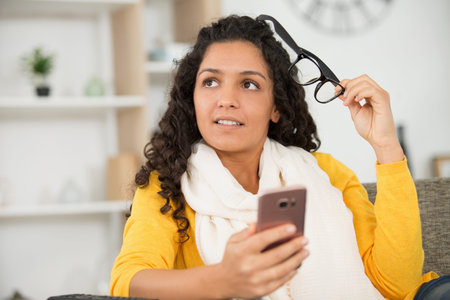 young woman holding her eyeglasses while using smartphone