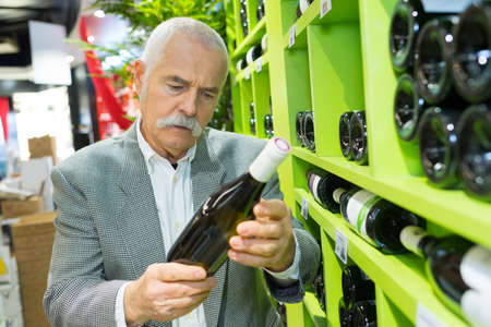 man in a supermarket choosing a wine bottleの写真素材
