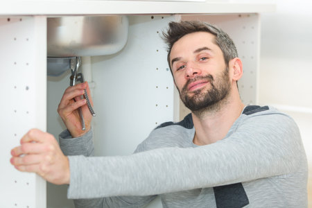male plumber installing kitchen sink using wrenchの写真素材