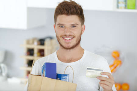 young man holding bag of groceries and credit cardの写真素材