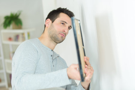 young man hanging a picture on the wallの写真素材