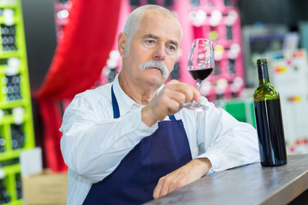senior wine store owner looking at red wine