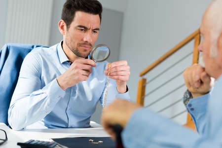 jeweler inspecting ring through magnifying glass in workshopの写真素材