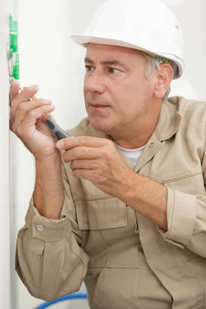 senior electrician using screwdriver on wall socketの写真素材