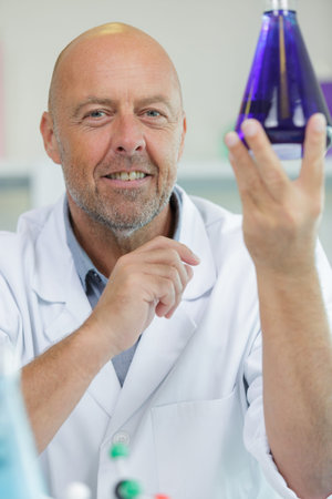 positive mature scientist showing a violet flask