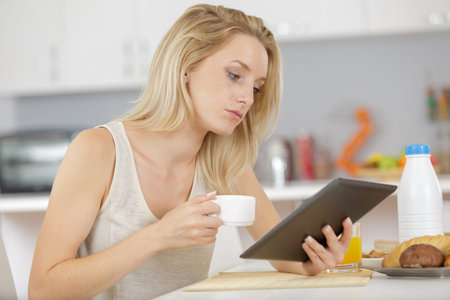 woman smiling at kitchen table with coffee and tabletの写真素材