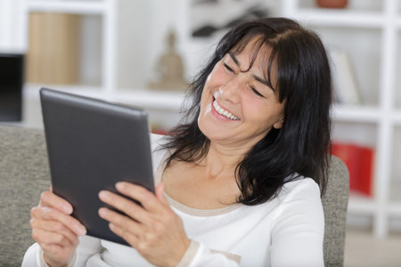 mature brunette woman sitting on sofa using digital tablet