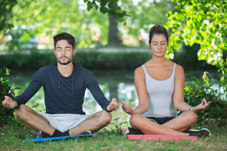 young couple doing yoga in park at morningの写真素材
