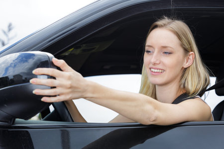 female driver adjusting car mirror