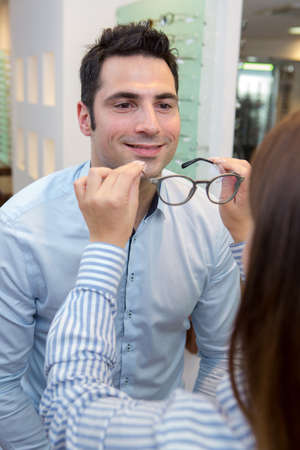 smiling man trying on glasses in optical storeの写真素材