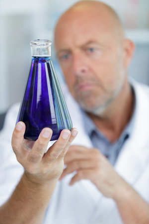 mature lab worker holding a violet flask