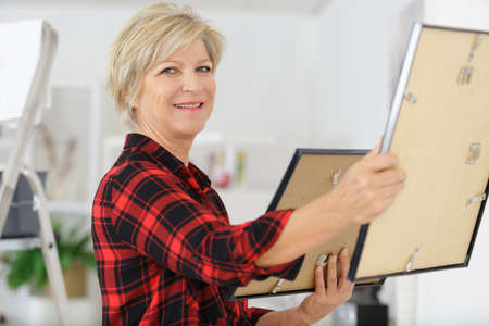 senior female artist hanging picture in studioの写真素材