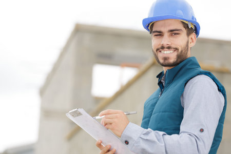 happy builder in hardhats with clipboard outdoors