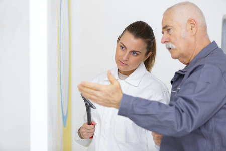 supervisor explaining to apprentice how to prepare wall with scraper