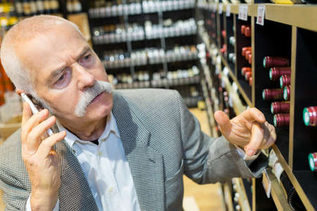 man analyzing a bootle of red wine in a supermarketの写真素材