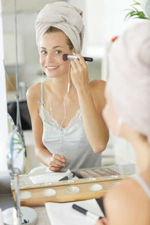 young beautiful woman applying makeup on face by brushの写真素材