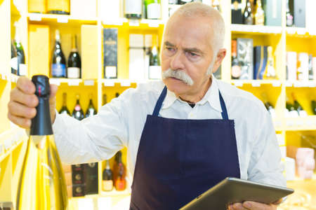senior shop assistant in wine department holding digital computerの写真素材