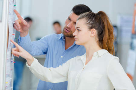 young man and woman pointing at bulletin boardの写真素材