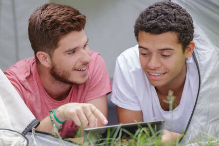 two young men layed in tent looking at tabletの写真素材
