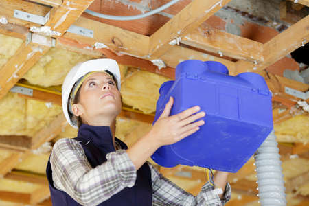 woman builder fitting ventilation box into roof spaceの写真素材
