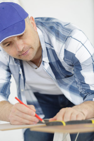 Carpenter measures with the tape measure and pencil on wood