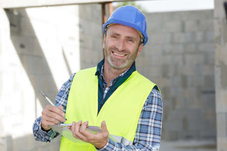 confident engineer holding blueprint outdoors in construction siteの写真素材