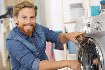 Happy young husband man doing laundry at homeの写真素材