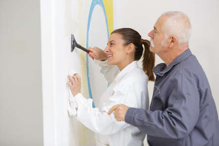 senior craftsman guiding apprentice scraping wallの写真素材