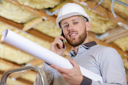 builder in helmet talking with phone with drawings