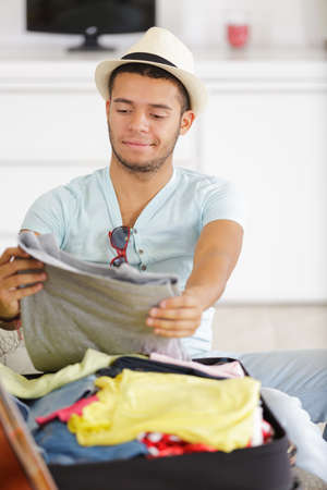 thoughtful young man packing luggage on bed for travelの写真素材