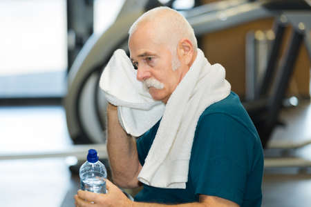 elderly tired man in a gym with towelの写真素材