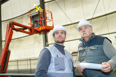 two male workers with cherry picker in background