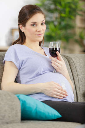smiling pregnant woman drink glass of wine at homeの写真素材