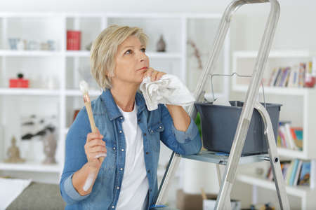 senior woman thinking before painting the wallの写真素材