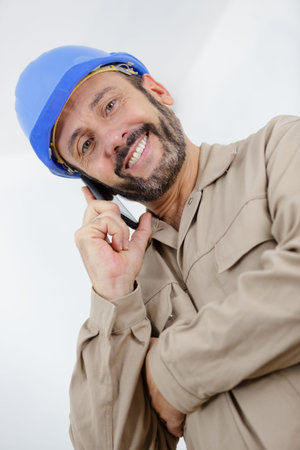 smiling man builder in hard hat using mobile phone