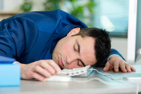 tired overworked man sleeping on keyboard in office at workの写真素材