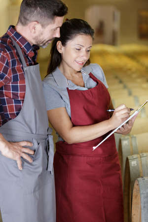 smiling girl with male worker in small winery cellarの写真素材