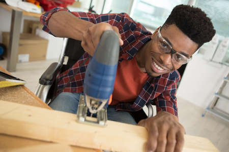 male carpenter in a wheelchair using a jigsawの写真素材