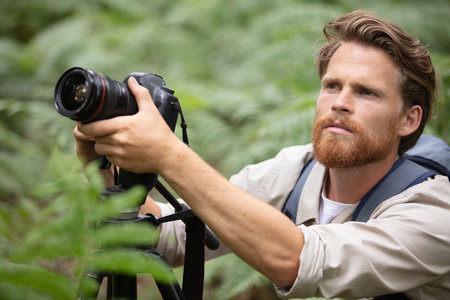 man with beard holds photocamera on green nature