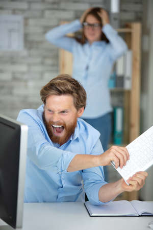 stressed businessman breaks the computer with keyboardの写真素材
