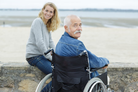 senior man in wheelchair with adult daughter looking at sea