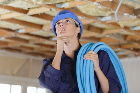 female builder holding cables while working on the ceilingの写真素材
