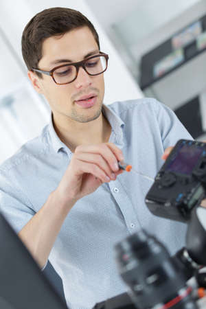 young confident technician is fixing and cleaning a digital cameralenseの写真素材