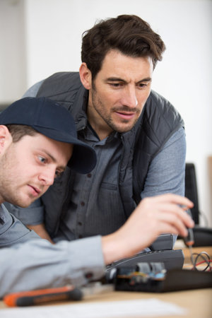 man and apprentice repairing broken smartphone in workshop