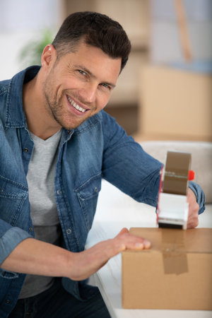 happy man wrapping a box while he is moving home