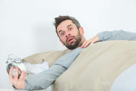 stunned man in bed holding alarm clockの写真素材