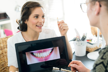 young orthodontist showing sample of teeth implant to patient