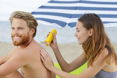 woman is applying sunscreen on the back of a manの写真素材