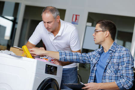 two plumber with clipboard fixing a washing machineの写真素材